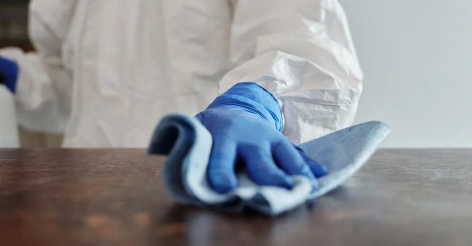 A close-up of a person's hand cleaning a table. This person is wearing a protective gear and glove.