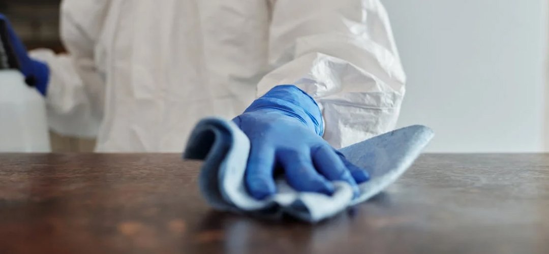 A close-up of a person's hand cleaning a table. This person is wearing a protective gear and glove.