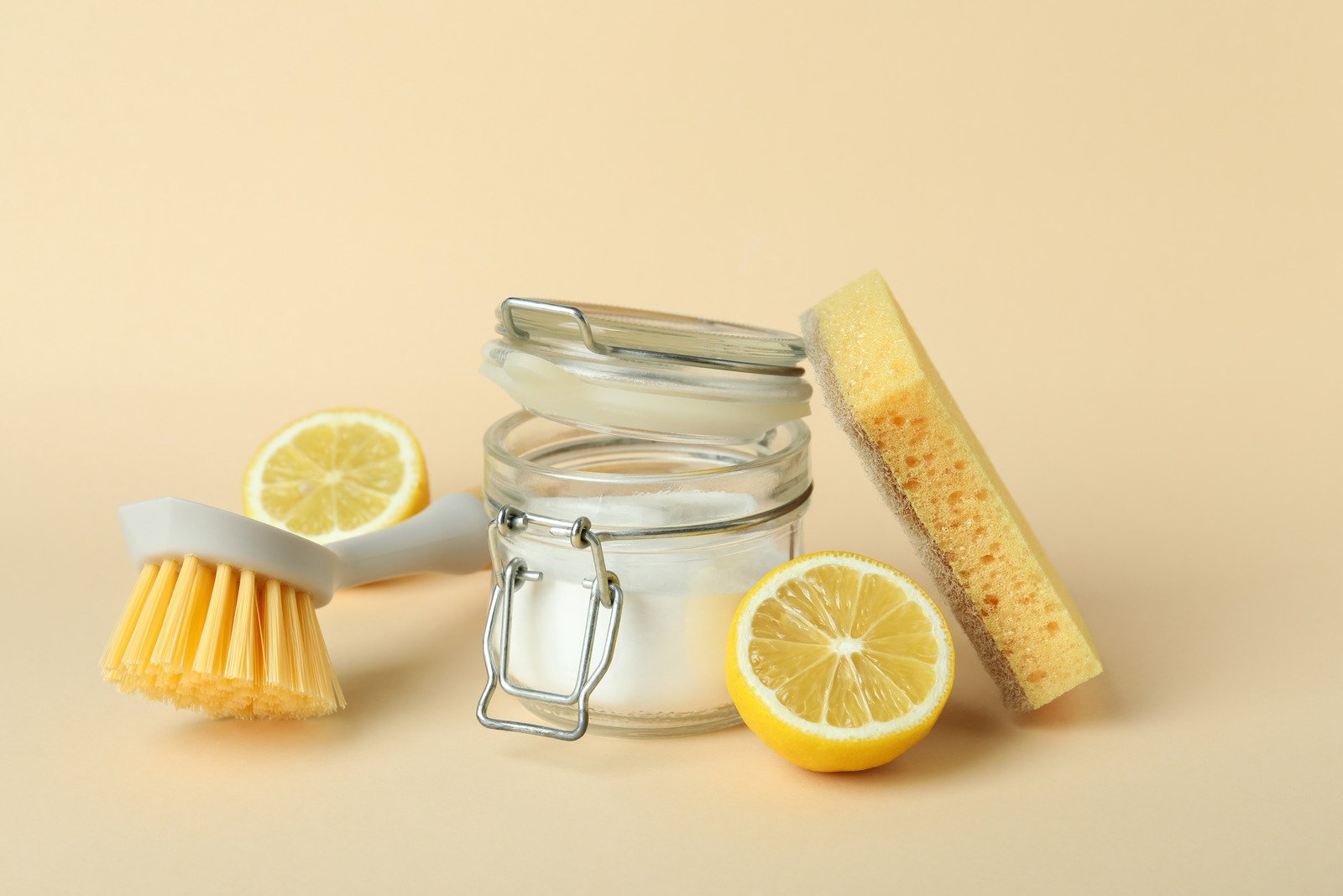 Jar of baking soda, lemons, brush, and sponge for natural cleaning. 