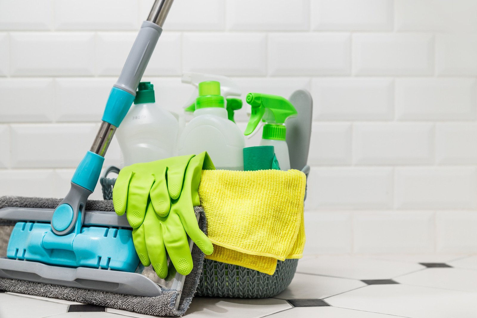 White mop with a bucket and cleaning supplies in a woven basket on the tile floor.