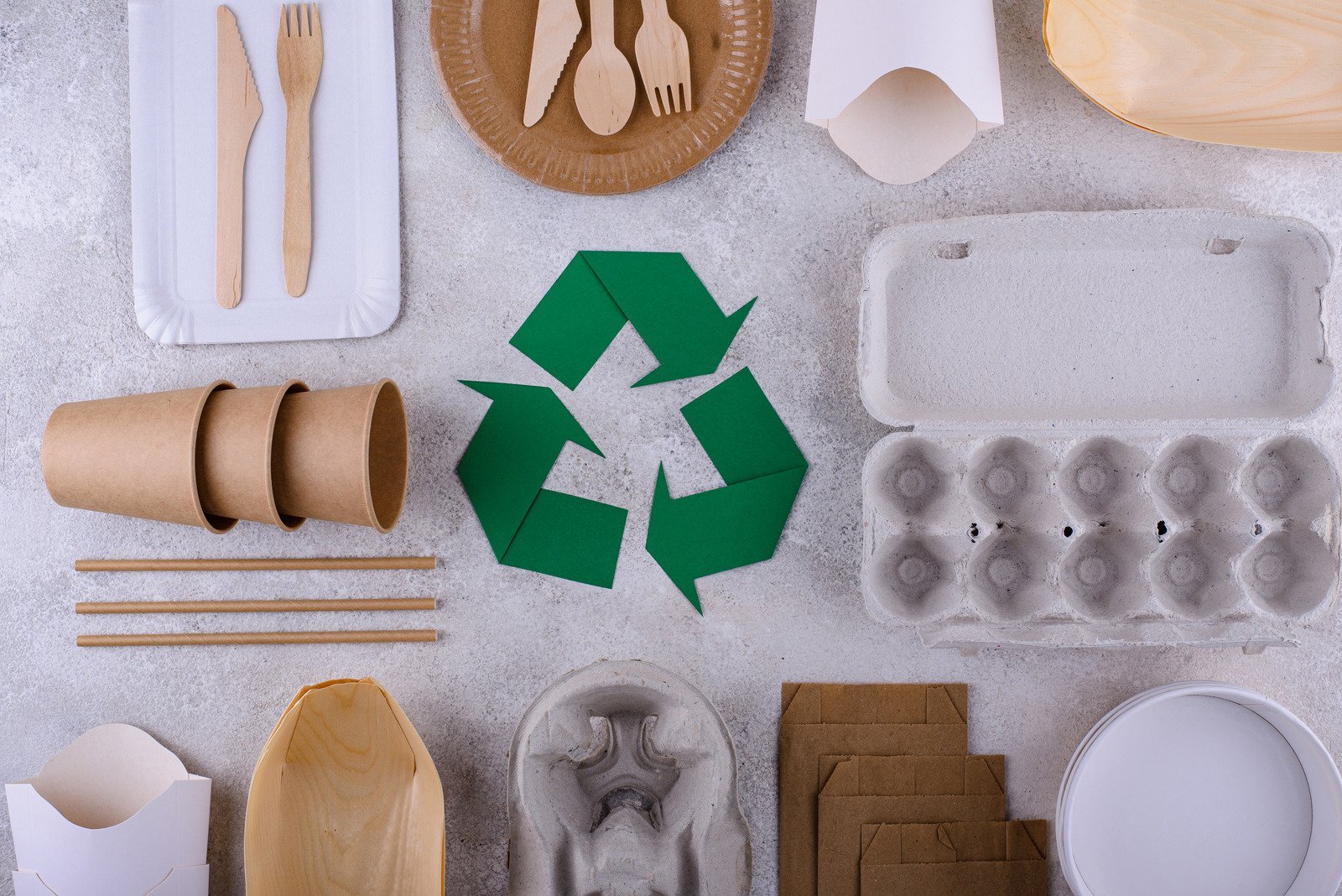 Universal recycling symbol surrounded by recyclable materials like plastic bottle, aluminum can, and paper. 