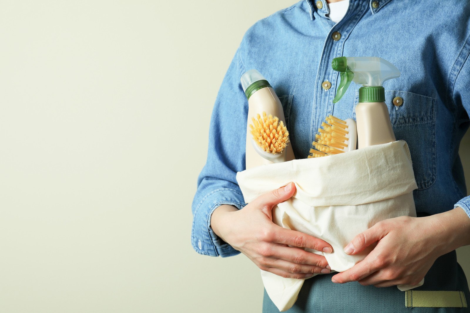 Woman wearing denim jacket holding a basket of eco-friendly cleaning products.