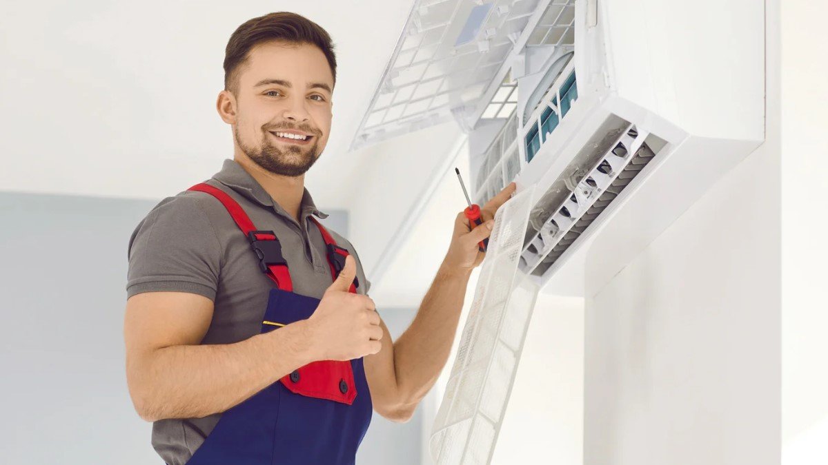 Happy young male contractor fixes an opened AC unit with a red screw driver.