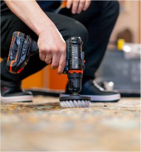 Close-up of a person using a drill brush attachment to clean a carpet, effectively removing stains and odors with precision.