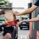 A fast-food worker hands a paper bag of food to a customer in a car at a drive-thru window, illustrating a convenient meal pickup process.