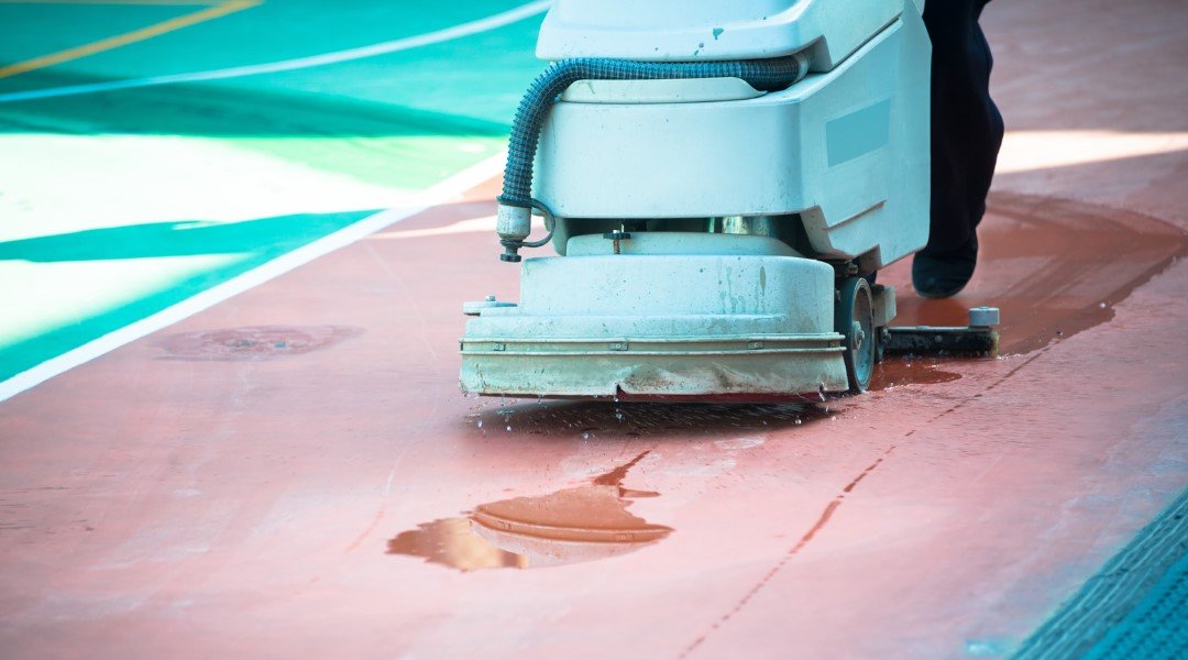 A close-up of a floor scrubber cleaning a sports court, removing dirt and water, ensuring a clean and safe playing surface.