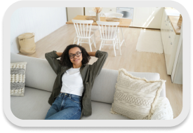 A woman relaxes on a couch in a clean and well-organized living space, enjoying the comfort provided by professional cleaning services.