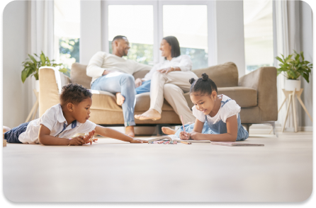 Two children play on a spotless living room floor while their parents relax on the couch, highlighting the benefits of residential cleaning services.