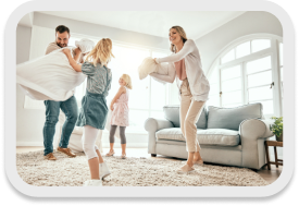 A cheerful family has a pillow fight in a bright, clean living room, showcasing the results of professional residential cleaning services.