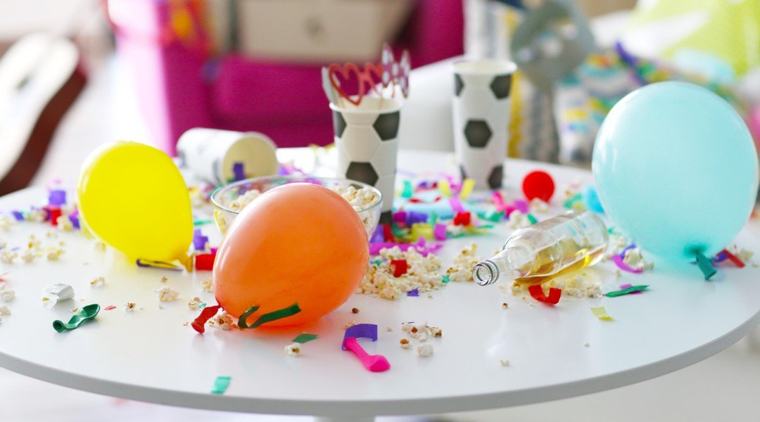 A table scattered with balloons, confetti, popcorn, cups, and an empty bottle, capturing the aftermath of a lively party.