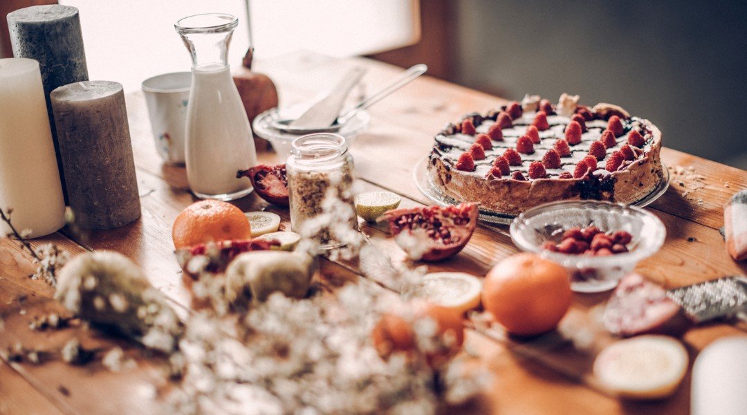 A rustic table setting with a berry tart, fresh fruit, milk jug, and candles, creating a cozy and inviting atmosphere.