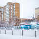 A snowy city scene with tall brick apartment buildings, frosted trees, and snow-covered fences, showcasing a typical winter day.